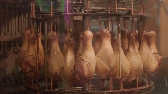 Roasted chicken drumsticks mounted on a rotating vertical grill rack for cooking.