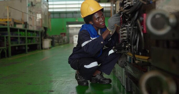 African woman technician crouching to check hydraulic fittings of a large injection mould