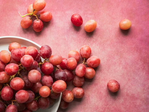 Bunches of ripe red grapes on a pink surface from above