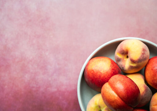 Bowl of ripe summer peaches and nectarines on pink background