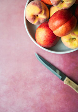 Bowl of peaches and nectarines with knife on pink background