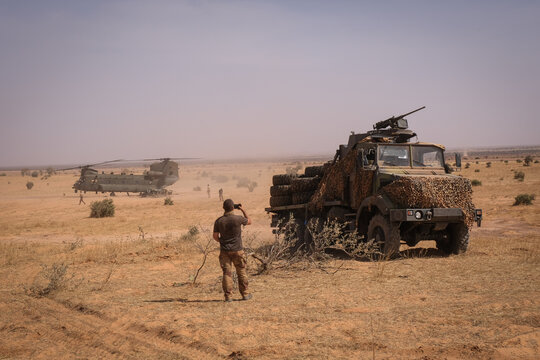 Armoured truck standing guard while a military helicopter waits in the desert in the Sahel near Tin-Akoff, Burkina Faso