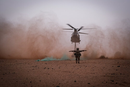 Marshaller standing firm as helicopter rotor wash swallows him in dust in the Sahel near Tin-Akoff, Burkina Faso