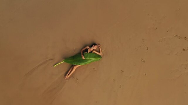 Woman Lying on a Banana Leaf on Sandy Beach Top View