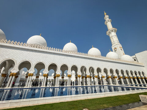 White marble domes and arcades of the Grand Mosque aligned above the water in Abu Dhabi, United Arab Emirates