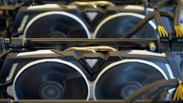 open frame mining rig Centered graphics card shows two rotating cooling fans with another GPU softly visible behind and yellow black PCIe wiring at the edge