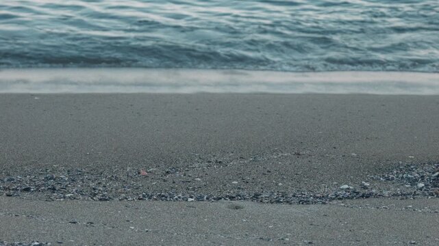 Close-Up of Small Waves Lapping Against a Blue-Gray Sandy Beach