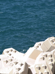 Fototapeta premium Concrete Tetrapod Breakwater Blocks Along Deep Blue Ocean Water