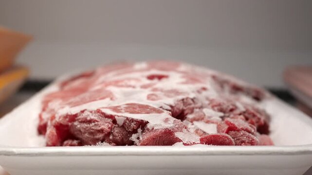 Frozen raw meat in white foam tray inside domestic freezer close up cinematic camera motion.