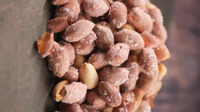 Salty roasted peanuts with skin spinning on wooden table for healthy snack and food concept.