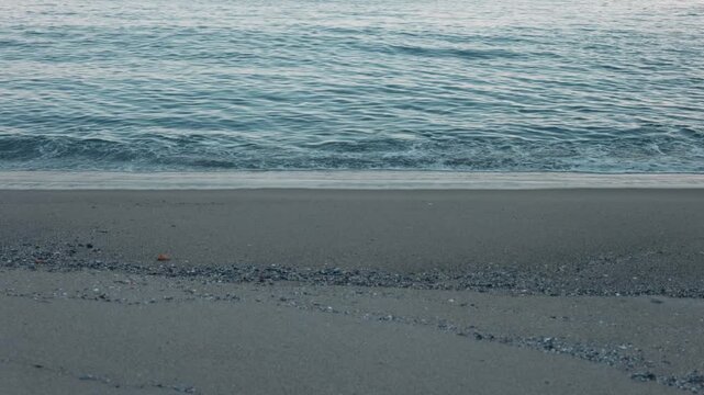 Close-Up of Small Waves Lapping Against a Blue-Gray Sandy Beach