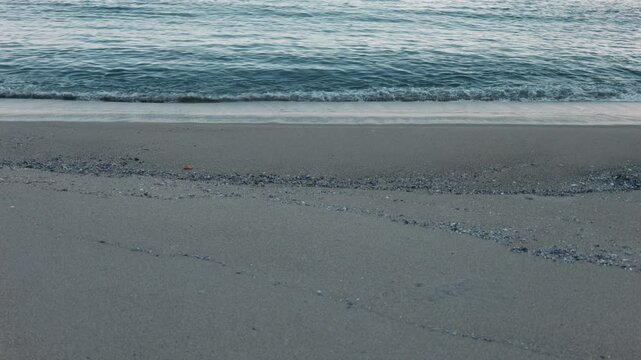 Close-Up of Small Waves Lapping Against a Blue-Gray Sandy Beach
