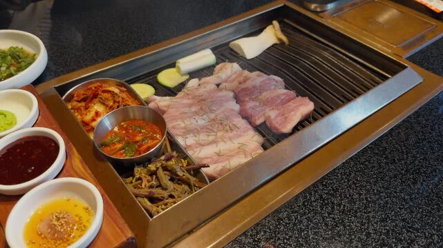 Korean BBQ Pork Belly Grilling on Charcoal Grill Table with Banchan Close-Up