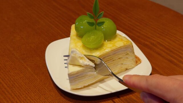 Hand Cutting Slice of Crepe Cake with Fork on White Plate Close-Up Dessert