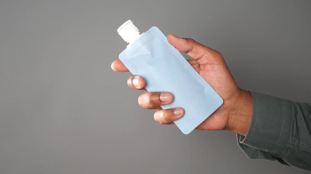 Hand holding small blue travel pouch with white cap against gray background.