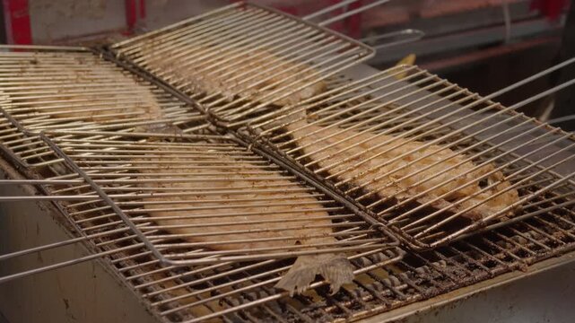 Raw fish is placed in metal grilling racks for cooking, set in a food preparation area.