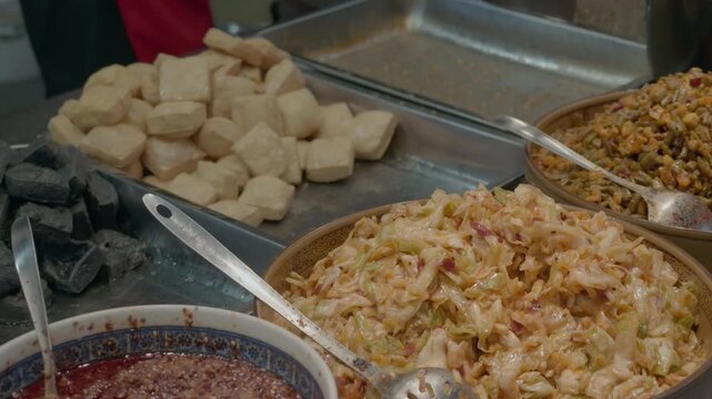 Various prepared fermented tofu dishes and condiments displayed on metal trays at a food stall.