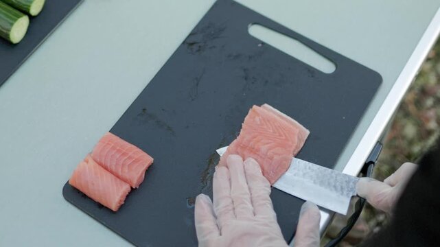 Sushi chef carefully slices fresh red fish into thin pieces with a sharp knife preparing ingredients for Japanese cuisine and traditional sushi dishes