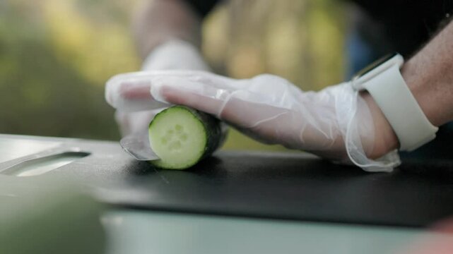 Skilled sushi chef finely slices a green cucumber with a sharp knife creating even pieces for roll filling during the preparation of fresh Japanese cuisine