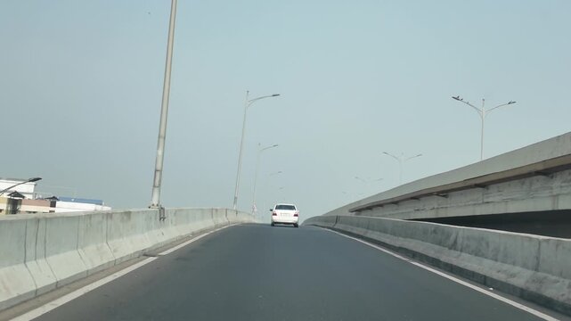 White car driving on an elevated highway or freeway road under bright daytime sky.