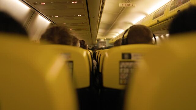 Rows of passengers relax in their seats inside a passenger aircraft during flight while soft warm cabin lights create a peaceful atmosphere for modern air travel