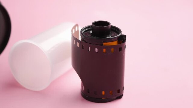 Camera film roll and lens on pink background with slow camera movement capturing details.