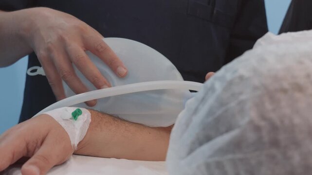 Anesthesiologist squeezing manual breathing bag valve mask to ventilate patient in operating room