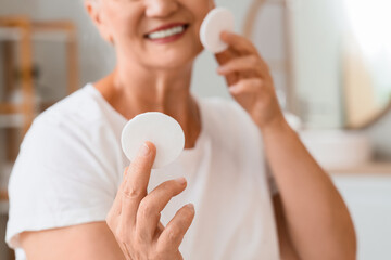 Healthy aging and skincare routine, senior woman cleaning face with cotton pad for skin rejuvenation and daily hygiene in a bright home bathroom © Pixel-Shot