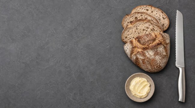Bread knife and artisanal loaf on stone countertop flat lay