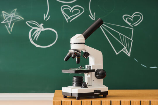 Stem education and scientific research, microscope on wooden desk with chalk drawings on green blackboard in classroom for school learning and discovery