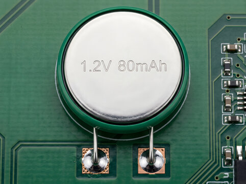 A 1.2v 80mah button cell battery on a green electronic circuit board.