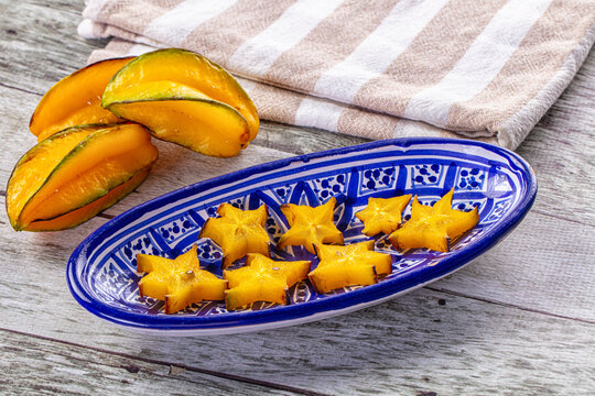 Striped kitchen towel beside whole and sliced carambola star fruit on blue patterned oval plate over rustic wood, fresh tropical fruit serve