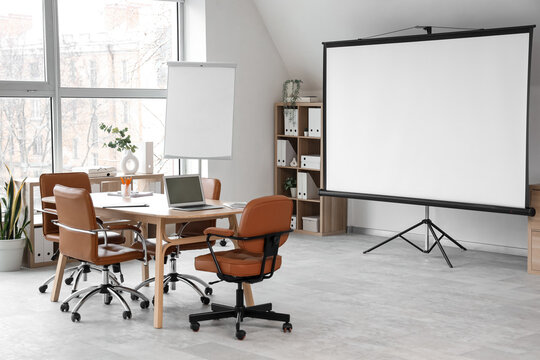 Corporate meeting room with blank projection screen, business presentation and team collaboration space in a modern office with laptop on wooden table