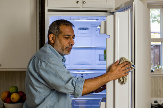 Middle Eastern man wiping inside of an empty refrigerator