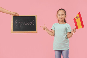 Spanish language learning and education, young girl holding flag of Spain and pointing at chalkboard with written text on a pink background © Pixel-Shot