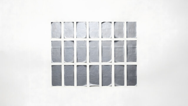 Grid of eighteen rectangular silver metallic foil strips arranged in three rows on a plain white studio background surface
