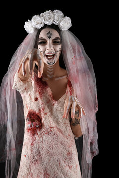 Halloween horror and death concept, scary zombie bride with skull makeup and bloody wedding dress reaching out in dark studio portrait