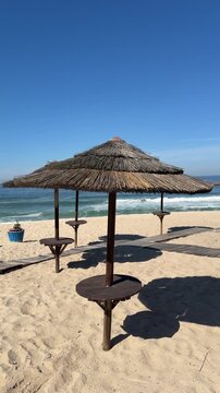 Rows of rustic tiki umbrellas stand on the white sand, overlooking a calm ocean.