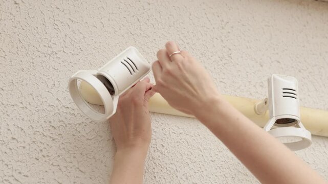 Person installs white track lighting fixtures on textured interior wall