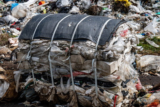 Large piles of household waste fill the area. Bundles of plastic bags and other trash are seen stacked together