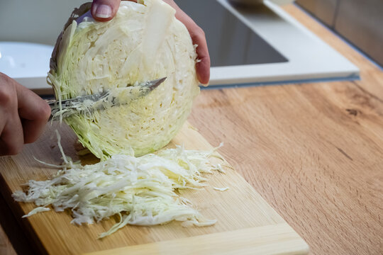 Chef hands shredding fresh green cabbage on wooden cutting board with knife