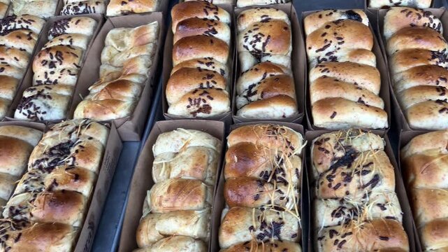 Close up view of rows of freshly baked sweet bread buns topped with chocolate sprinkles and cheese, neatly arranged in cardboard packaging boxes in a bakery.