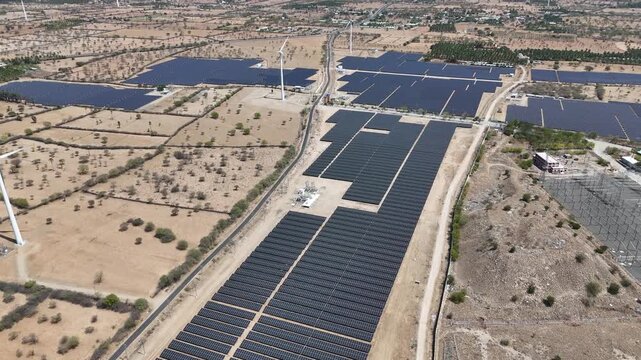 Cinematic aerial drone view of a large-scale solar power plant, showcasing thousands of photovoltaic panels arranged in organized rows across a vast arid landscape. Service roads, electrical infra
