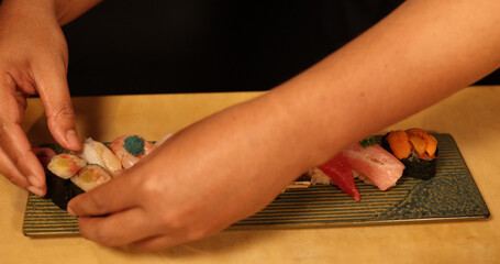 Hands Serving Fresh Nigiri and Maki Sushi on Ceramic Plate © blueringmedia