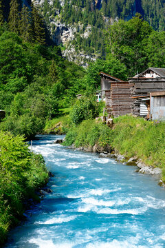 Malerischer Bergbach Sch&auml;chen mit t&uuml;rkisblauem Wildwasser und gestapeltem Holz am Ufer in Untersch&auml;chen, Kanton Uri, Schweiz