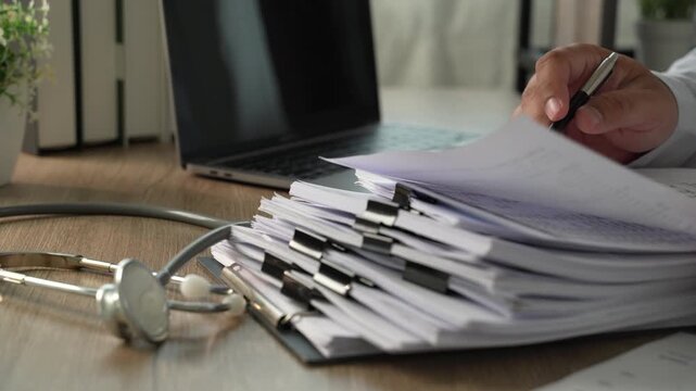 Hands sorting and turning stacked clipped documents on a desk, showing document management, file review and office administration workflow.