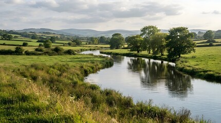 Obraz premium Calm river winding through green countryside with trees, meadows and hills