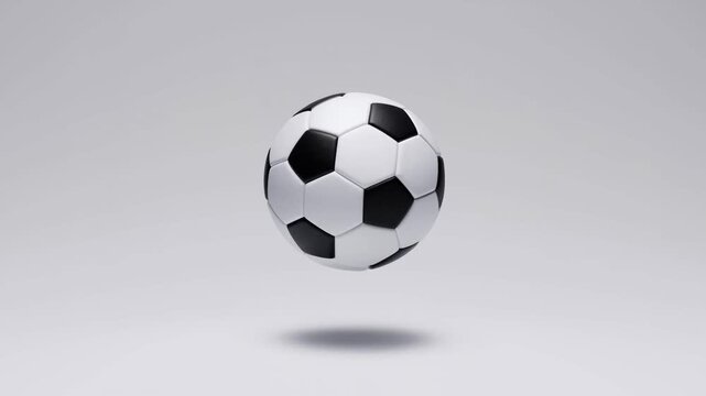 Slow motion tracking shot of soccer ball hovering rotating and descending over white studio background