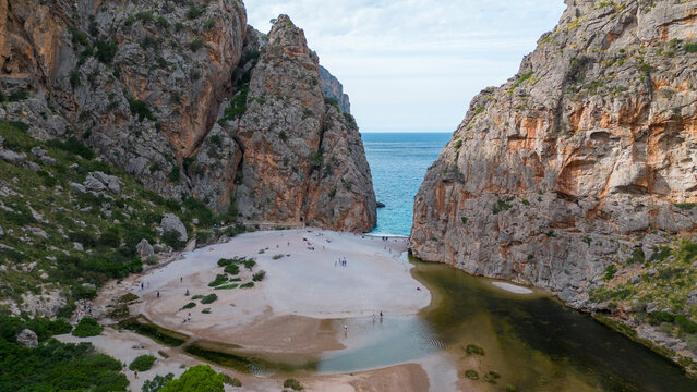 Aerial view of the small beach between towering orange limestone cliffs at the mouth of the Torrent de Pareis canyon at Sa Calobra on Mallorca, Spain