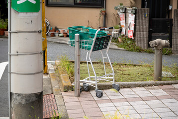 Shopping cart and green basket left abandoned outside a store on a sidewalk © TYAK_FACTORY
